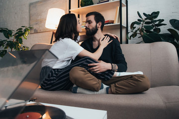 Fototapeta premium beautiful young couple sitting on couch and listening to vinyl record in living room