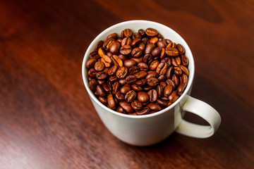 Fototapeta premium Roasted Coffee beans in a white mug cup isolated on a rustic wood table 