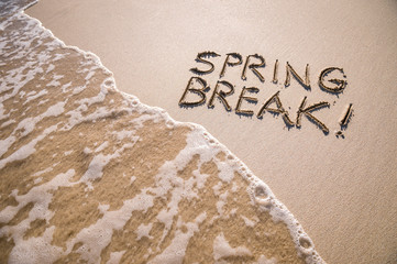 Excited Spring Break message handwritten on the smooth sand of an empty beach with an oncoming wave - 250600893