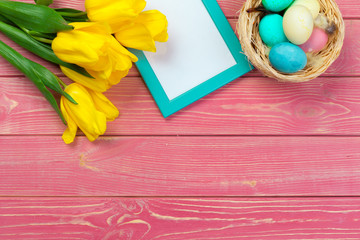 Easter concept. Wooden frame with easter eggs and tulips on colorful background