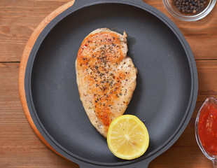 Fried chicken breast with half a lemon in a pan,