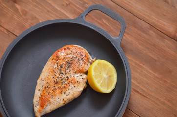 Fried chicken fillet is lying on a frying pan with a lemon