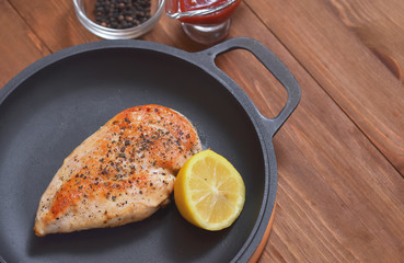 Fried chicken fillet is in a frying pan with lemon and sauce