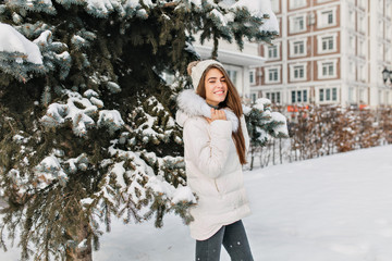 Enchanting blonde woman in white jacket and black jeans posing during walk in winter park. Outdoor...
