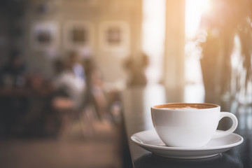 Cappuccino cup on the table with blur people in coffee shop background, vintage tone 