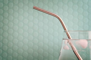 Glass of water with ice and a stainless steel reusable straw on a dotted emerald green background
