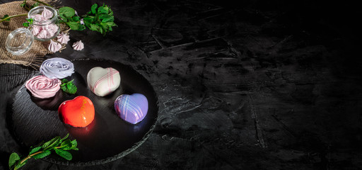 Three sweet desserts in the shape of a heart heart with mirror glaze on dark background with copy...