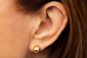 health, people and hearing concept - close up of senior woman ear with golden earring
