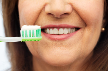 dental care and hygiene people concept - close up of smiling senior woman with toothbrush brushing her teeth over white background