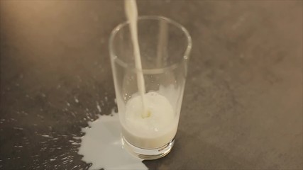 Glass of spilling milk. Milk is poured past the glass. Beautiful glass tumbler on a gray table. View from above. - Powered by Adobe
