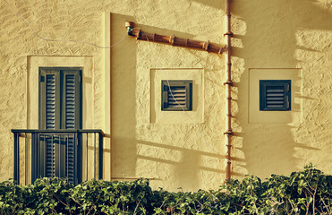 Yellow rugged wall with shutters and old ceramic gutter, color toned picture.