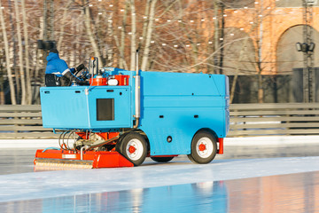 Outdoor photo of special machine leveling ice rink in motion, side view/ ice maintenance machine clean and pours ice before the game, ice resurfacer at work, public skating rink, hockey stadium.