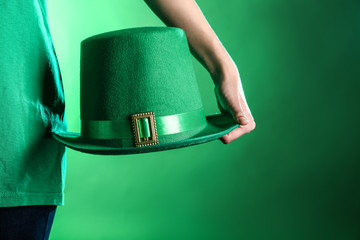 Young woman holding green hat on color background. St. Patrick's Day celebration