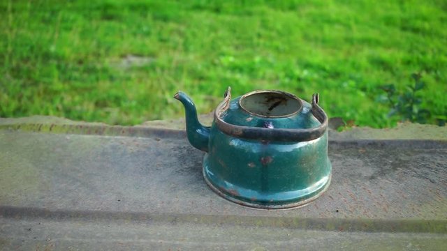 Still life with an old rusty kettle on a background of metal surface and green grass.
