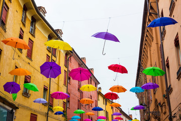 Colorful umbrellas floating in the sky above the ancient UNESCO listed town centre of Ferrara,...