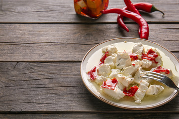 Plate with tasty feta cheese, chili pepper and olive oil on wooden table