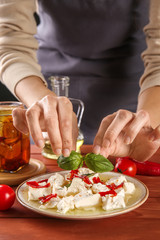 Woman putting herbs onto plate with tasty feta cheese and olive oil on table