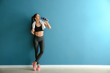 Sporty young woman with bottle of water near color wall - Powered by Adobe