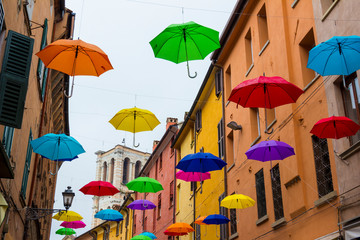 Colorful umbrellas floating in the sky above the ancient UNESCO listed town centre of Ferrara, Italy. - obrazy, fototapety, plakaty
