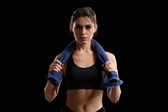 Sporty young woman with towel on dark background
