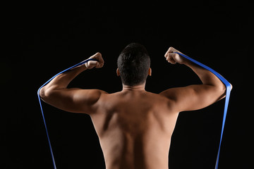 Sporty young man training with resistance band against dark background