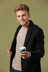 Fashionable young man with cup of coffee on color background