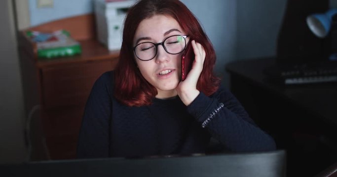 european girl in glasses talking on the phone near the computer