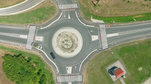 Truck is moving closer to traffic circle and waits for another car just passing traffic circle. Truck continuoes driving intp traffic circle.