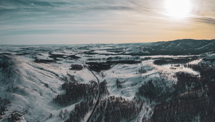 Aerial; drone panoramic view of winter mountain landscape with blue sky and clouds; sunny day in russian countryside; snow fields and mixed forest with birches and pine trees; local ski resort Bannoe