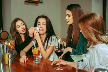 Stress. Female friends having a drinks at bar. They are sitting at a wooden table with cocktails....