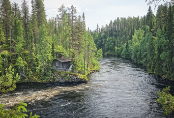 Scandinavian landscape with an old fisherman's hut along the Oulankajoki river at the Oulanka National Park in Kuusamo, Finland. Scenic view of the northern nature and the flowing water in the stream.