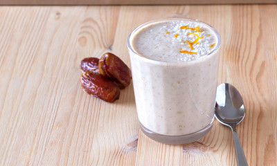 Healthy organic date, banana and apple milk smoothie powdered shreded coconut and orange zest. Fresh diet breakfast. Wooden background. Selective focus.