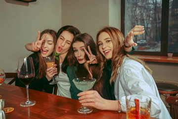 Female friends having a drinks at bar. They are sitting at a wooden table with cocktails. They are wearing casual clothes.