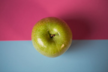 Close up of a green apple on blue and pink background.