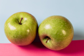Close up of a green apple on blue and pink background.