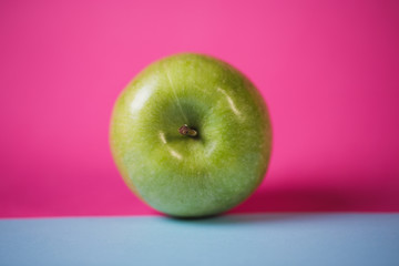 Close up of a green apple on blue and pink background.