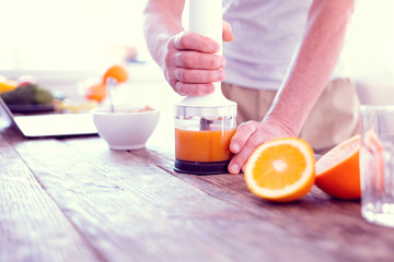 Close up of man using his modern blender while squeezing morning orange juice
