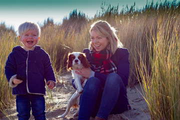 A mother and son with pet dog at the beach smiling