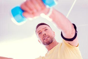 Bearded man wearing yellow shirt holding blue barbells while working on his body