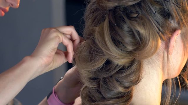 Makeup artist and hairdresser are preparing bride before wedding. Hairdresser-stylist with short stylish hairstyle applies makeup, makes false eyelashes, paints lips, curls girl, spectacular lighting