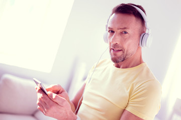 Handsome blue-eyed man feeling relaxed while listening to music using earphones