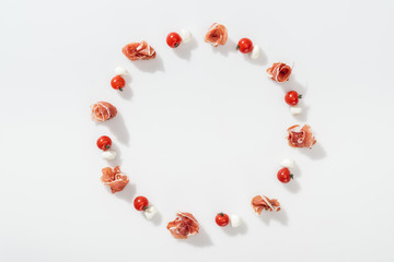 top view of tasty prosciutto near red cherry tomatoes and mozzarella cheese on white background