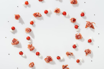 flat lay of tasty prosciutto near red cherry tomatoes, mozzarella cheese and peppercorns on white background