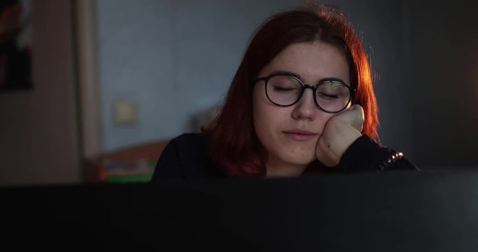 girl in glasses is sleeping behind the monitor. Close-up. Eyes closed. evening