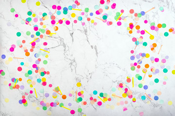 Colorful confetti frame on white marble texture with natural pattern. Festive birthday template background. Flat lay. Top view