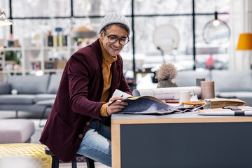 Joyful good-appealing adult fancy designer selecting fabric samples in office