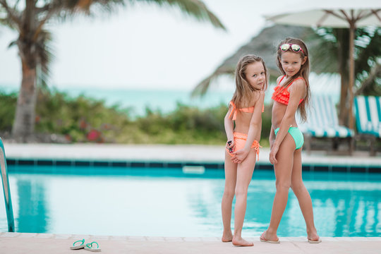 Adorable little girls having fun in outdoor swimming pool on summer vacation