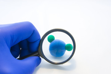 Analysis or laboratory testing of water for quality and safety concept photo. Researcher looking through magnifying glass on model of water molecule. Idea for chemical and bacteriological analysis