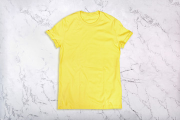 Yellow t-shirt on white marble background. Flat lay. Top view