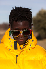 retrato de chico negro con cazadora amarilla y gafas de sol de colores al aire libre